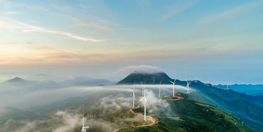 Aerial shot of wind turbines by windy road on cloudy mountaintop. 